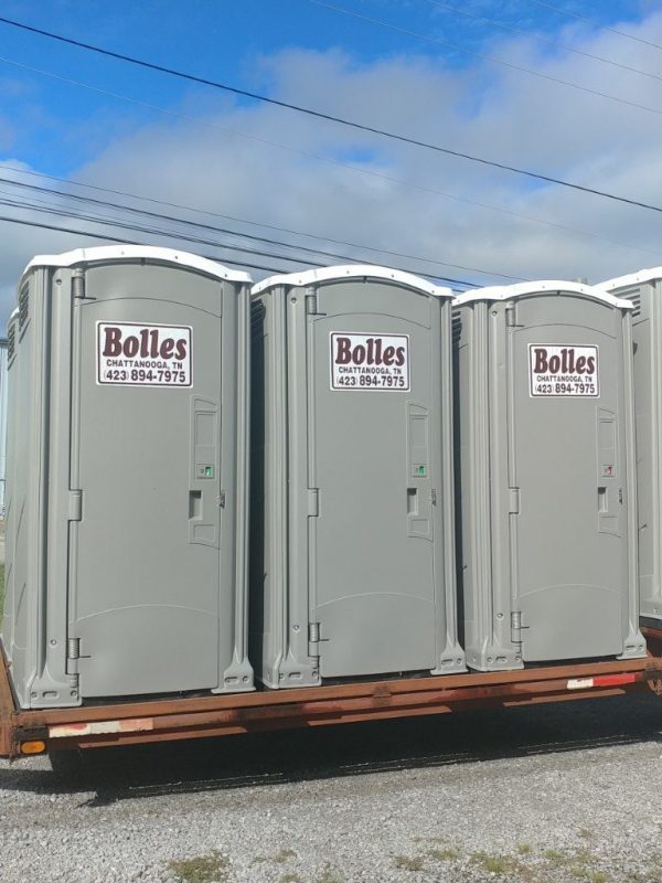 A row of portable toilets displayed on a trailer, each marked with a sign reading Bolles Chattanooga, TN 423 894-7975, set against a backdrop of blue skies and scattered clouds.